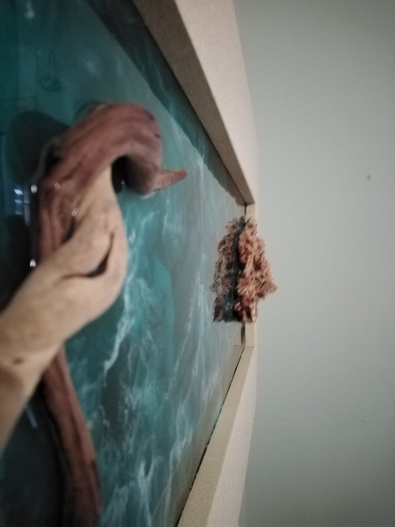May include: A wooden sculpture of an octopus with a light brown color, mounted on a wall with a blue and white ocean-themed background. A small, textured, coral-like object is also mounted on the wall.