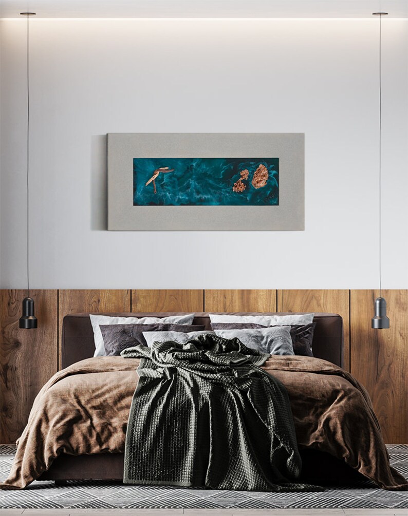 May include: A bedroom scene featuring a bed with brown bedding and a dark green blanket. Above the bed is a framed artwork with a teal background and gold accents. The headboard is made of wood panels, and the room has a modern design.