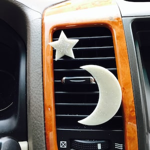 May include: White star and crescent moon car air freshener hanging from a car's air vent.
