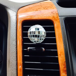May include: A silver disco ball air freshener hanging from a car's air vent.
