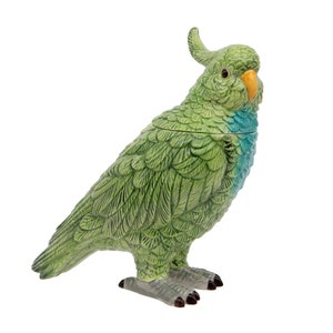 May include: A green ceramic parrot ornament with an orange beak and a crest. The bird features detailed feather patterns and stands on grey feet. This decorative item is likely a figurine for display.