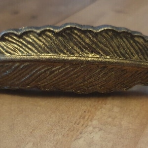 May include: A gold-coloured metal feather-shaped door pull or cabinet knob.