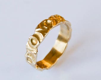 May include: A gold ring with a textured, circular design. The ring is made of a smooth, polished metal.
