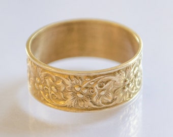 May include: A gold band ring with a floral design. The ring is wide and has a smooth, polished finish.