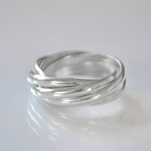 Puede incluir: Un anillo de plata con un diseño único entrelazado. El anillo está hecho de múltiples bandas que están retorcidas e interconectadas para crear un patrón complejo e interesante.