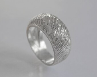 May include: A silver ring with a textured, hammered finish. The ring is wide and has a rounded shape.