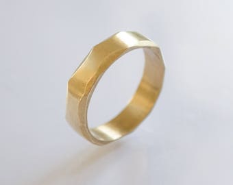 May include: A gold-colored ring with a textured, faceted design. The ring is made of metal and has a simple, modern style.