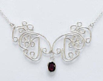 May include: A silver necklace with a delicate, intricate design featuring a small, dark red gemstone pendant.