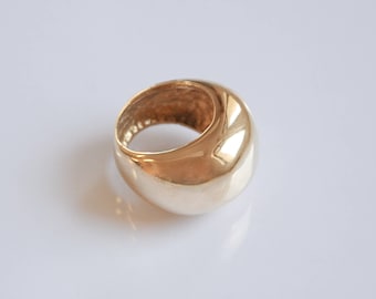 May include: A gold-colored, domed ring with a smooth, polished surface. The ring has a rounded shape and a hollow interior. The ring is likely made of metal and reflects light, creating highlights and shadows.