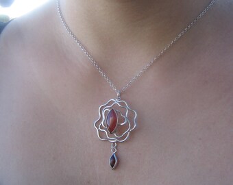 May include: A silver chain necklace with a pendant featuring a red gemstone set in a silver flower design.