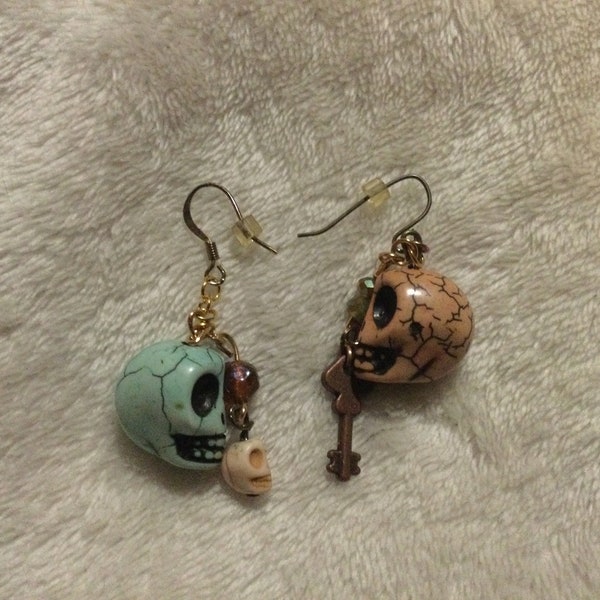 Teal skull with ivory skull and iridescent brown glass bead earring. Pink howlite stone skull, bronze key, and iridescent