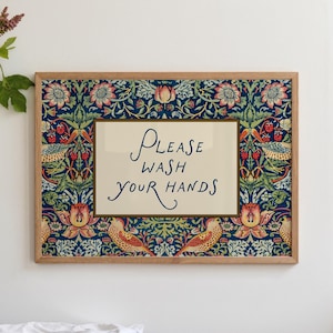 May include: A framed print with a wooden border. The print has a cream-coloured centre with the words "Please Wash Your Hands" in blue script. The border is a dark blue floral pattern with birds and berries.