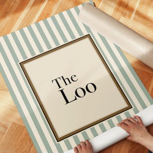 Sage green striped “The Loo” bathroom wall art print being unrolled showing vintage style typography