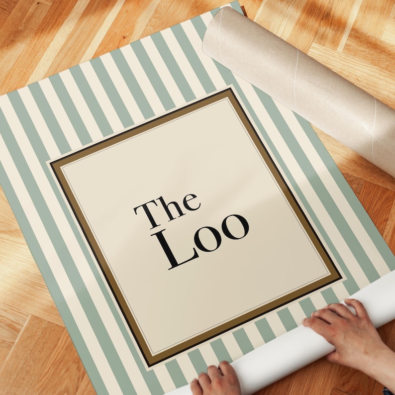 Sage green striped “The Loo” bathroom wall art print being unrolled showing vintage style typography