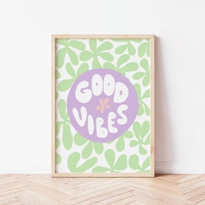 May include: A framed print with a light purple circle on a white background with green leaf shapes. The circle has the text "GOOD VIBES" in white with a small pink flower in the center.