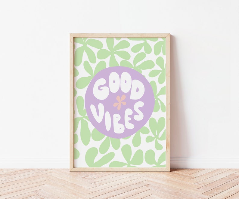 May include: A framed print with a light purple circle on a white background with green leaf shapes. The circle has the text "GOOD VIBES" in white with a small pink flower in the center.