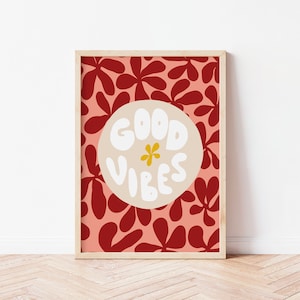 May include: A framed print with a red and pink floral pattern. The print features a white circle with the text "GOOD VIBES" in a white, bubbly font. A yellow flower is in the center of the circle.