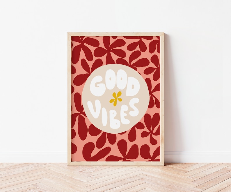 May include: A framed print with a red and pink floral pattern. The print features a white circle with the text "GOOD VIBES" in a white, bubbly font. A yellow flower is in the center of the circle.