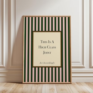 May include: A framed print with a striped background of dark green and pink. The print features the text "THIS IS A HIGH CLASS JOINT" and "Act Accordingly" in a serif font, set against a cream-colored background.