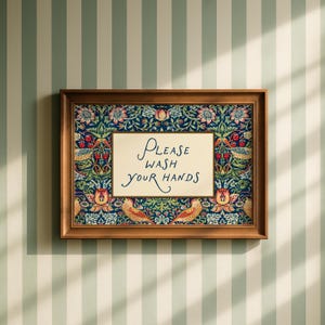 May include: A framed sign with the words "PLEASE WASH YOUR HANDS" in elegant script. The sign is set against a floral patterned background with a dark blue base and a wooden frame. The sign is hanging on a striped wall.