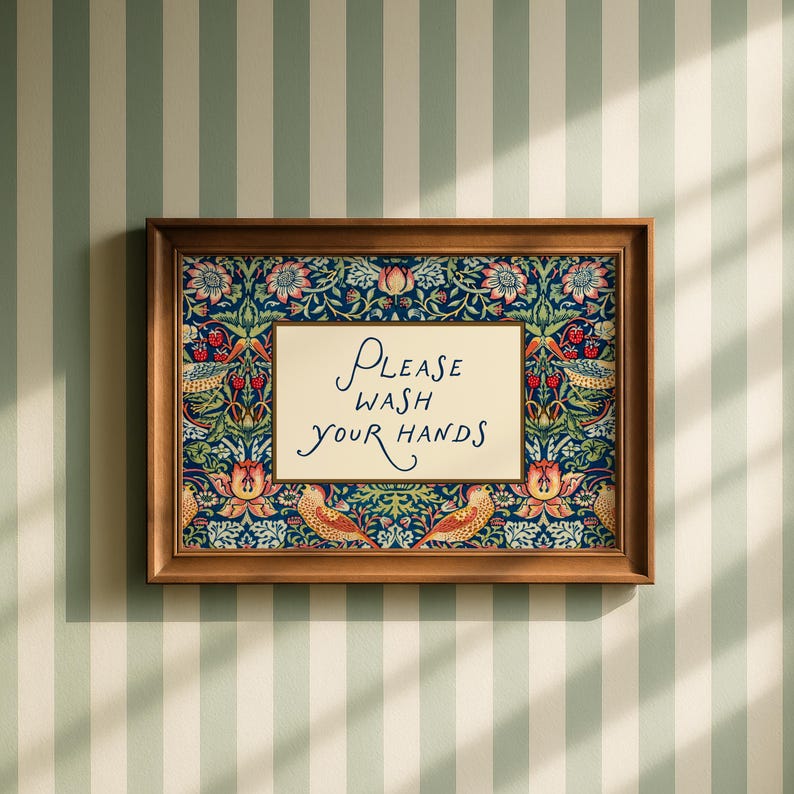 May include: A framed sign with the words "PLEASE WASH YOUR HANDS" in elegant script. The sign is set against a floral patterned background with a dark blue base and a wooden frame. The sign is hanging on a striped wall.