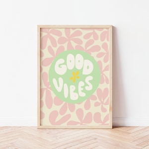 May include: A framed print with a light green circle on a background of pink and cream abstract floral shapes. The circle contains the text "GOOD VIBES" in white with a yellow flower in the center.