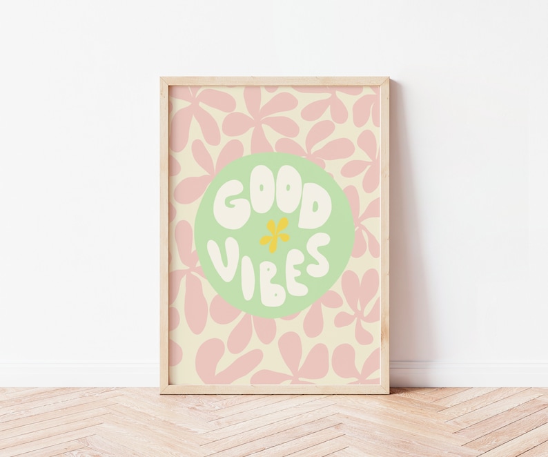 May include: A framed print with a light green circle on a background of pink and cream abstract floral shapes. The circle contains the text "GOOD VIBES" in white with a yellow flower in the center.