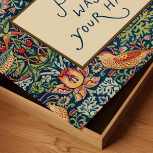 May include: A wooden tray featuring a detailed floral design in shades of blue, green, orange, and pink. The tray holds a cream card with the handwritten text "I WAS YOUR HAIR". The tray rests on a wooden surface.