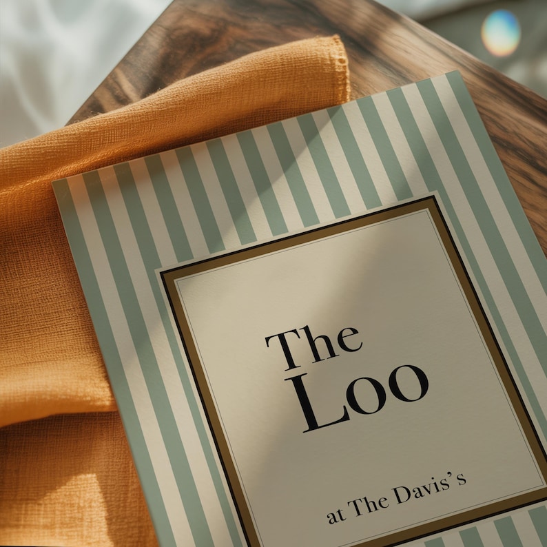 Close up of personalised “The Loo” print with sage green stripes and vintage typography on a styled surface