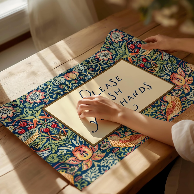 May include: A rectangular mat with a floral and bird design in blue, green, and peach tones. The centre has a cream rectangle with the words "PLEASE WASH HANDS" in dark blue script. The mat is on a wooden surface.