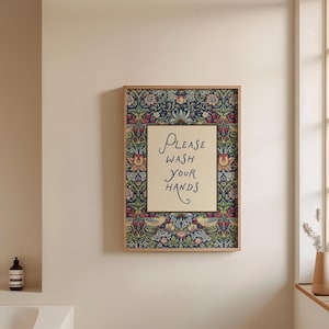 May include: Framed wall art with a floral border in blue, red, and yellow. The centre has the text "Please Wash Your Hands" in script on a cream background. The frame is light brown. Ideal for a bathroom or washroom.