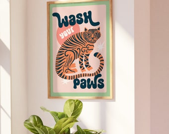 May include: A framed art print featuring a stylized tiger illustration in orange and black stripes. The artwork includes the text "Wash your paws" in a playful font, set against a pink and green background. The print is in a wooden frame.