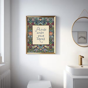 May include: A framed print with the text "PLEASE WASH YOUR HANDS" in a bathroom. The artwork has a gold frame and a floral design with a navy blue background. A round mirror and sink are also visible in the bathroom.