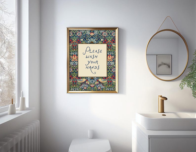 May include: A framed print with the text "PLEASE WASH YOUR HANDS" in a bathroom. The artwork has a gold frame and a floral design with a navy blue background. A round mirror and sink are also visible in the bathroom.