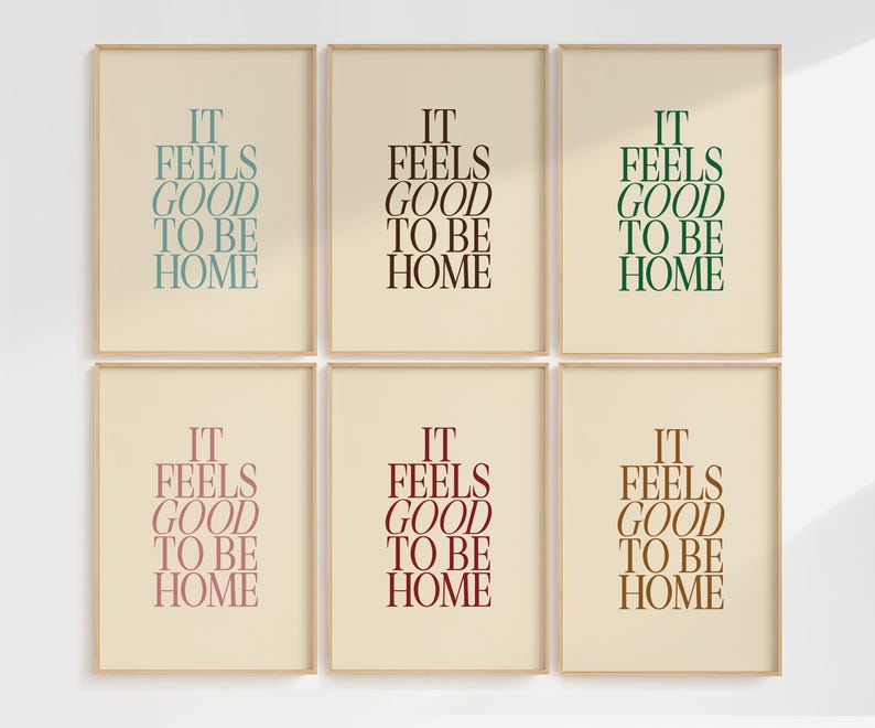 May include: Six framed art prints with the text "IT FEELS GOOD TO BE HOME" in various colors: teal, black, green, pink, burgundy, and brown. The text is centered on a cream-colored background, framed in a light wood.
