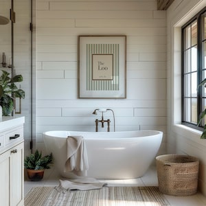Framed sage green striped “The Loo” bathroom wall art displayed above a freestanding bath in a bright modern bathroom
