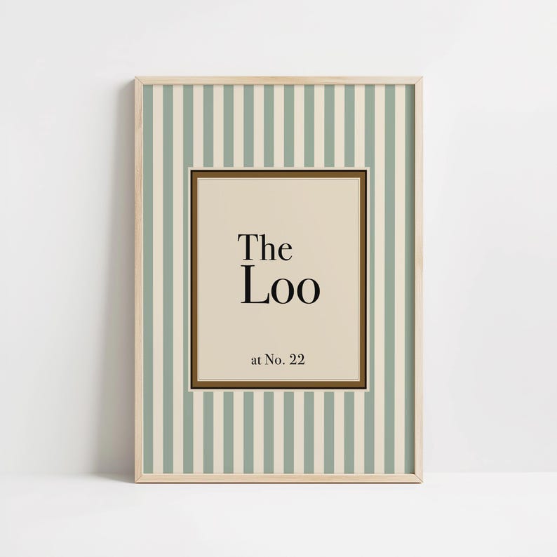 May include: Framed wall art with a light wood frame. The artwork features a striped background in white and pale green. The center has a beige rectangle with the words "The Loo" and "at No. 22" in black text.