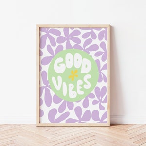 May include: A framed print with a purple and white floral pattern. The print features a green circle with the text "GOOD VIBES" in white with a yellow flower in the center.