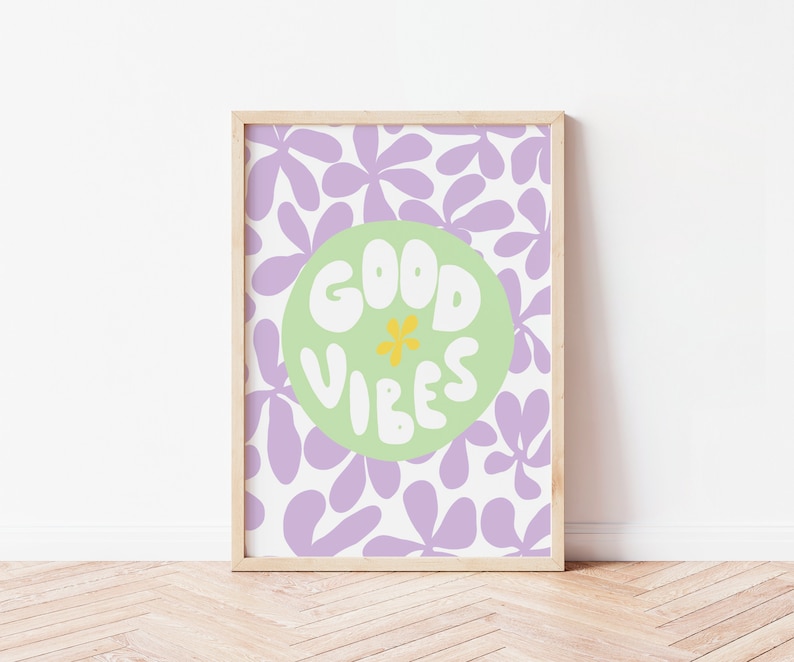 May include: A framed print with a purple and white floral pattern. The print features a green circle with the text "GOOD VIBES" in white with a yellow flower in the center.