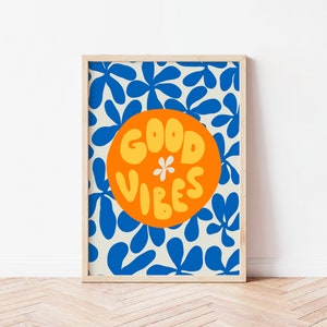 May include: A framed print with a white background and a blue floral pattern. A large orange circle with the text "GOOD VIBES" in yellow letters is in the center of the print.