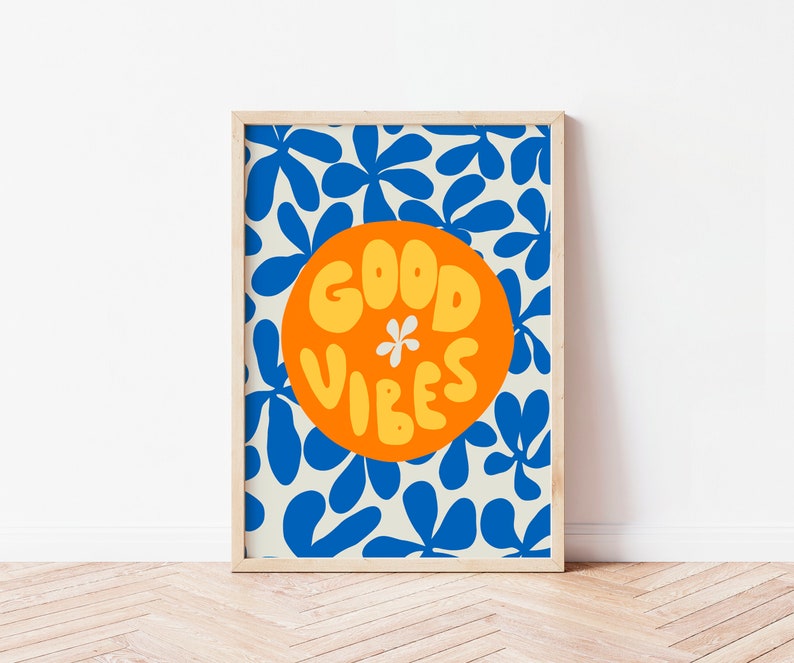 May include: A framed print with a white background and a blue floral pattern. A large orange circle with the text "GOOD VIBES" in yellow letters is in the center of the print.