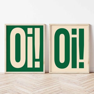 以下が含まれることがあります： 緑色の背景に白い太字で「Oi！」と書かれた額装されたプリントが2枚。フレームは明るい木の色です。