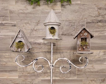 May include: White metal birdhouse stand with three birdhouses. The birdhouses are made of wood and have a distressed white finish. The stand has a scrolled design and a three-legged base.