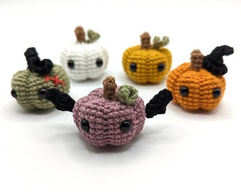 May include: Five crocheted pumpkins in different colors, including white, orange, green, and purple. Each pumpkin has a black button for eyes and a stitched-on stem.