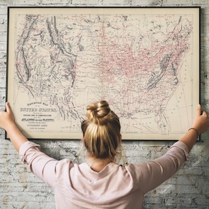 Könnte beinhalten: Eine gerahmte Vintage-Eisenbahnkarte der Vereinigten Staaten mit einem detaillierten Netzwerk von Linien in Rot und Schwarz. Die Karte wird von einer Person in einem rosa Hemd vor einer weißen Backsteinmauer gehalten.