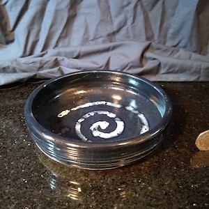 May include: A dark blue ceramic bowl with a white spiral design. The bowl has a slightly raised rim.