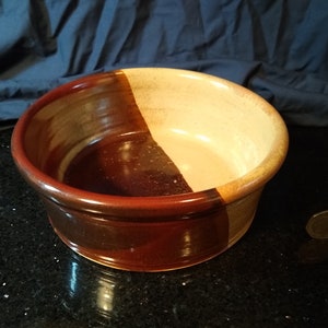 Op de afbeelding: Een keramische kom met een bruine en beige glazuur. De kom is in tweeën gedeeld, met aan de ene kant donkerbruin en aan de andere kant lichtbeige.