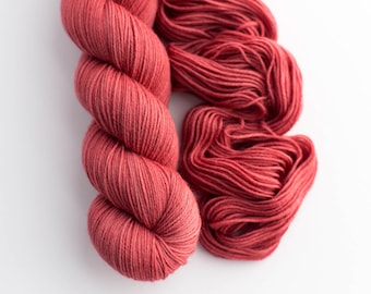 May include: Two skeins of coral-colored yarn are displayed against a white background. One skein is tightly wound, while the other is loosely arranged. The yarn appears soft and suitable for knitting or crocheting projects.