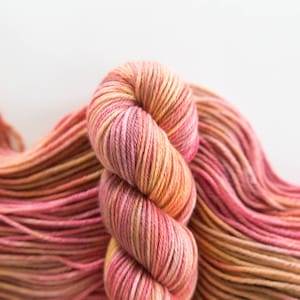 May include: A skein of pink and orange yarn with a gradient of color. The yarn is soft and fluffy, and it is perfect for knitting or crocheting.