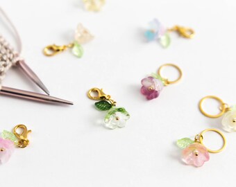 May include: Assortment of colorful flower-shaped stitch markers with gold rings and clasps. The markers are made of glass and have a delicate, feminine design.